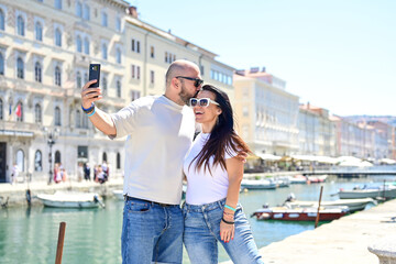 Fototapeta premium Trieste ,Italy, Canal Grande .Happy smiling couple of tourists making photos near Canal Grande at Trieste .Concept of Italian gastronomy and travel. Italian couple having fun together