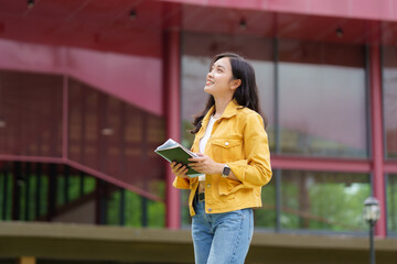 Smiling student holding book and looking up at university building