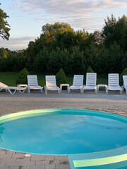 Tranquil outdoor pool area with white sun loungers surrounded by lush greenery. Relaxing summer...