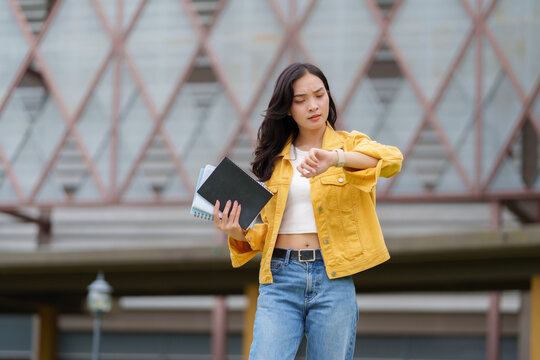 Impatient student checking time while holding books in university campus