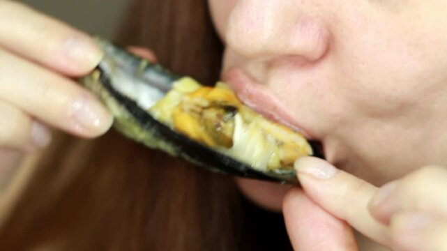 Close-up of a woman eating mussels. The woman's mouth bites the mussel meat from the shell