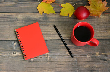Cozy Fall Morning Scene with a red cup of Coffee, Notebook and Autumn Leaves
