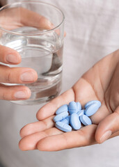 Woman in white t-shirt holding blue pills in cupped hand and water glass in hand closeup