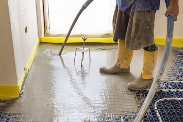 Man pouring concrete over floor heating installation in a new building. Modern construction system