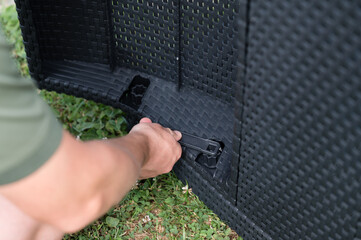 Person assembling outdoor furniture. A hand uses a tool to secure a piece.