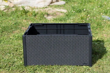 Empty raised garden bed ready for planting. Dark gray plastic construction, sits on green grass.