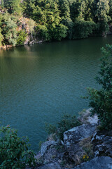A serene river, framed by dense green trees and rocky cliffs, flows peacefully under a summer sky.
