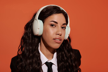 Young student embodies modern aesthetic with headphones against vibrant orange backdrop