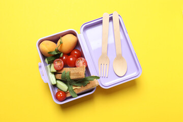 lunchbox with snacks, fruits, vegetables and water, as well as school supplies on a yellow...