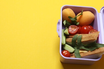 lunchbox with snacks, fruits, vegetables and water, as well as school supplies on a yellow...