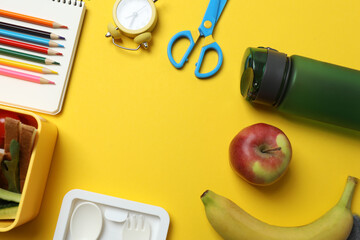 lunchbox with snacks, fruits, vegetables and water, as well as school supplies on a yellow...