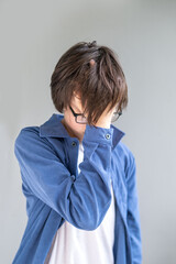 young Sad Teen boy in blue jacket, overwhelmed teenager hiding face, emotional reaction facepalm,...