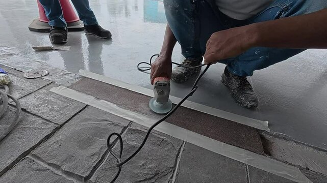 Uneven concrete patching is being ground smooth by a construction worker using an electric grinder. Safety is the top priority for this meticulous work.