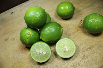 Stacked of fresh green limes on a rustic wooden surface, with two halves showing the juicy, citrus...
