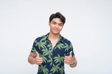 Confident Southeast Asian teenager in Hawaiian shirt smiling with double thumbs up gesture,...