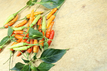 A vibrant pile of colorful chilies in red, orange, and green shades on a rustic wooden background....