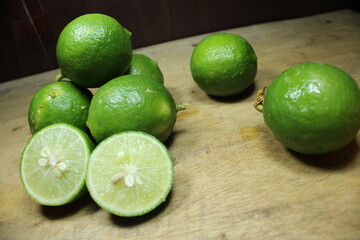 Stacked of fresh green limes on a rustic wooden surface, with two halves showing the juicy, citrus...