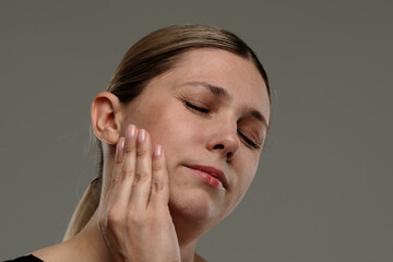 Woman with Closed Eyes Holding Cheek in Discomfort