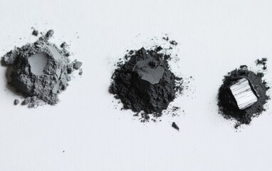 Three piles of dark gray and light gray powder on a white surface