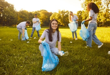 Portrait of a happy young woman with gloves and trash bag collecting plastic garbage in the summer...