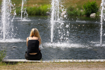 A lonely young woman with blond hair sits by a city fountain