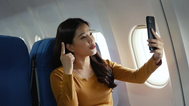 Woman making video call during airplane travel, smiling while connecting with someone through smartphone during international flight