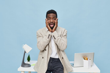 Frustrated young man with surprised expression, holding face with hands, standing at home office...