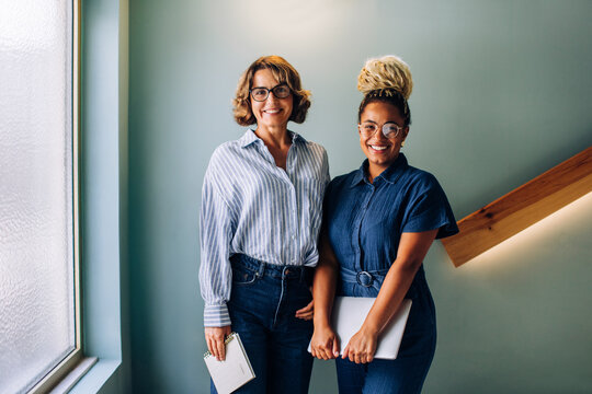 Two women standing together smiling in a casual office environment - Powered by Adobe
