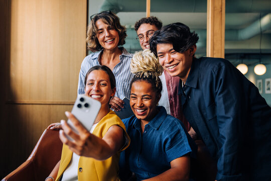 Group of diverse colleagues smiling and taking a selfie indoors - Powered by Adobe