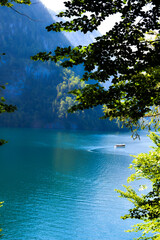 A beautiful lake lies calm and clear, surrounded by dense trees that reflect on the water’s...