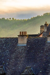 Tile roofs and chimneys of medieval rural houses in a village with misty hills illuminated by the sunset light.