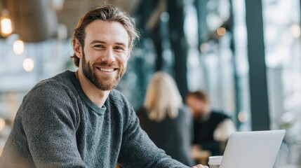 Friendly young man working on laptop in modern office with colleagues and bright lighting.