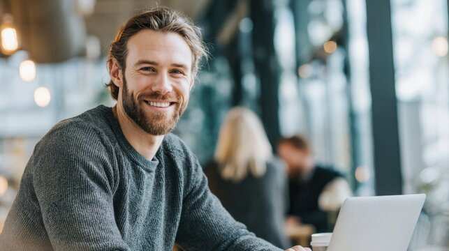 Friendly young man working on laptop in modern office with colleagues and bright lighting. - Powered by Adobe