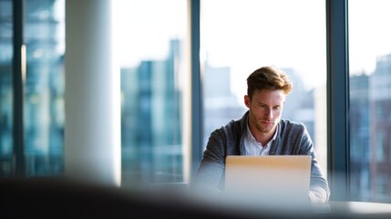 Businessman working on laptop at modern office with large windows and city view.