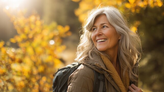 Smiling mature woman hiking outdoors in autumn landscape with colorful trees and sunny weather.