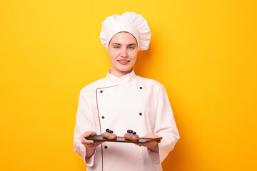 Confectioner in uniform holding delicious eclairs on orange background