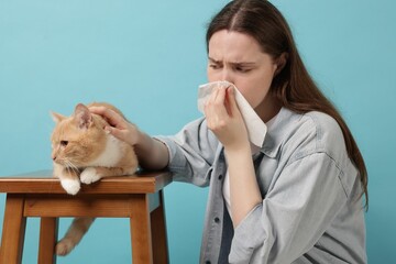 Woman suffering from allergy with her cat on light blue background