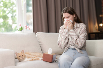 Woman suffering from allergy with her cat on sofa at home