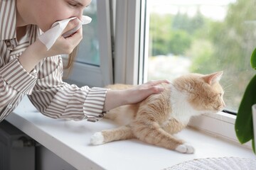 Woman suffering from allergy with her cat near window at home, closeup
