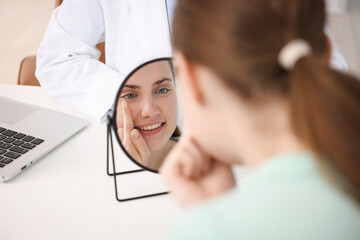 Young woman putting on contact lenses at table near mirror in ophthalmologist office, selective...