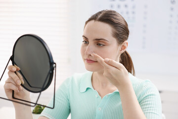 Young woman putting on contact lenses near mirror in ophthalmologist office