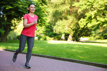Sporty woman with armband running in park, space for text