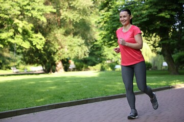 Sporty woman with armband running in park, space for text