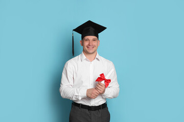 Happy student with diploma after graduation on light blue background