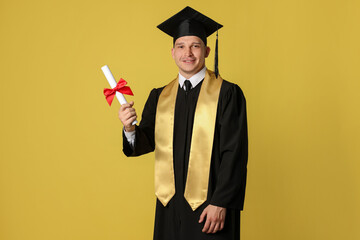 Happy student with diploma after graduation on yellow background