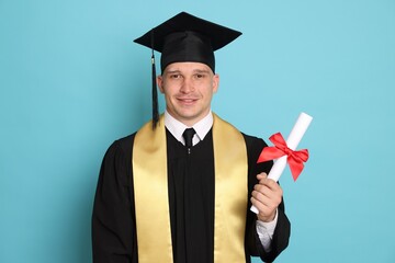 Happy student with diploma after graduation on light blue background