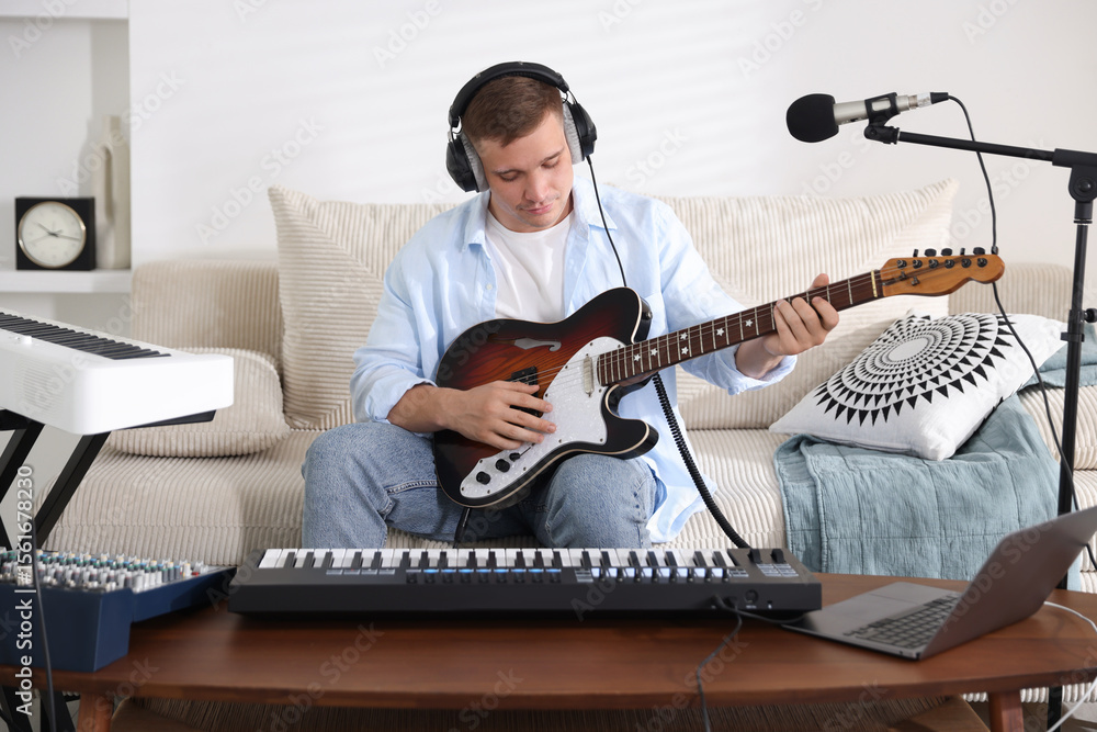 Poster man in headphones working with guitar and midi keyboard at table in home studio