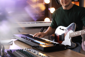 Man working with MIDI keyboard and guitar at table, closeup