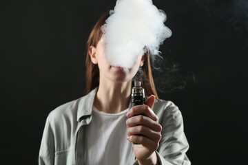 Woman using electronic smoking device on black background