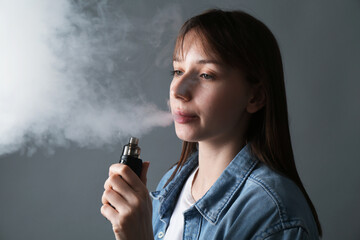 Woman using electronic smoking device on grey background